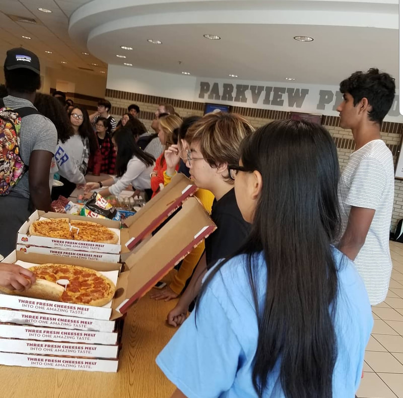 Three students hand out pizza to JCL members.